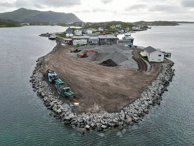 Landfylling og anleggsarbeid på molo, med maskiner og grus i havneområde.