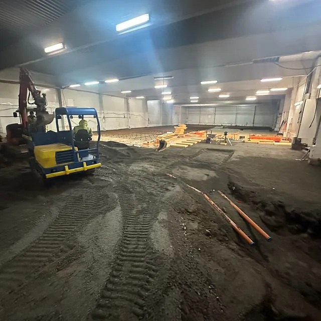 Innendørs anlegg med store steiner og gravemaskiner som bryter opp betonggulv.