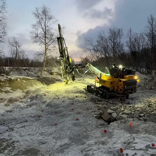 Borerigg jobber i steinete og snødekt terreng med røde markører for sprengning.