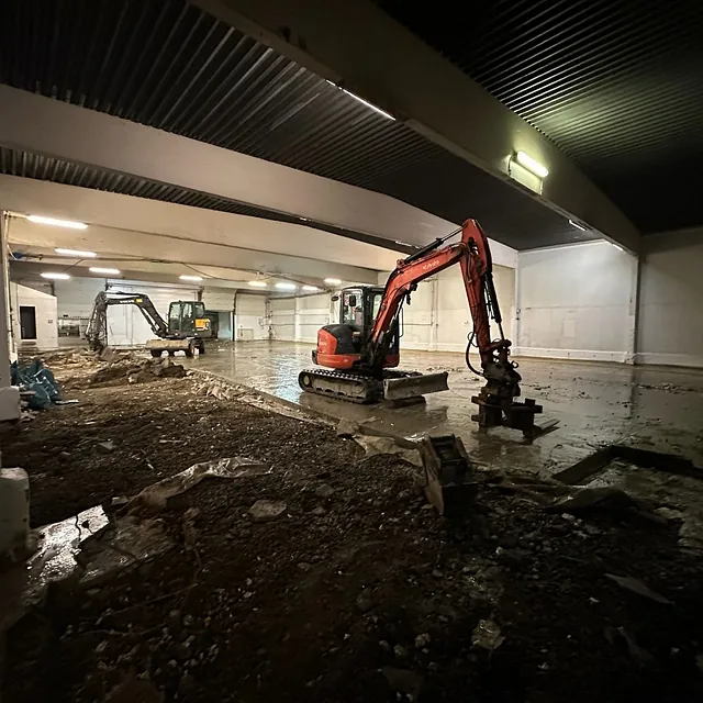 To minigravere i en stor industrihall, gulvet er delvis gravd opp for grunnarbeid.