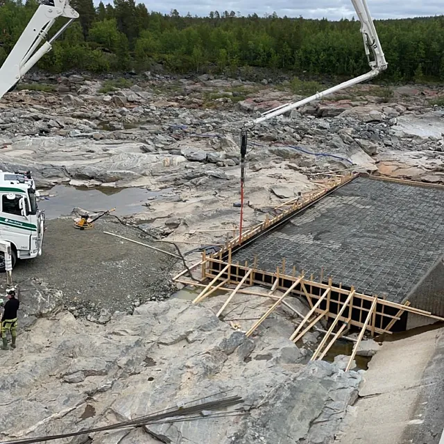 Betongstøping i fjellterreng, med pumpebil og forskaling over et elveleie.
