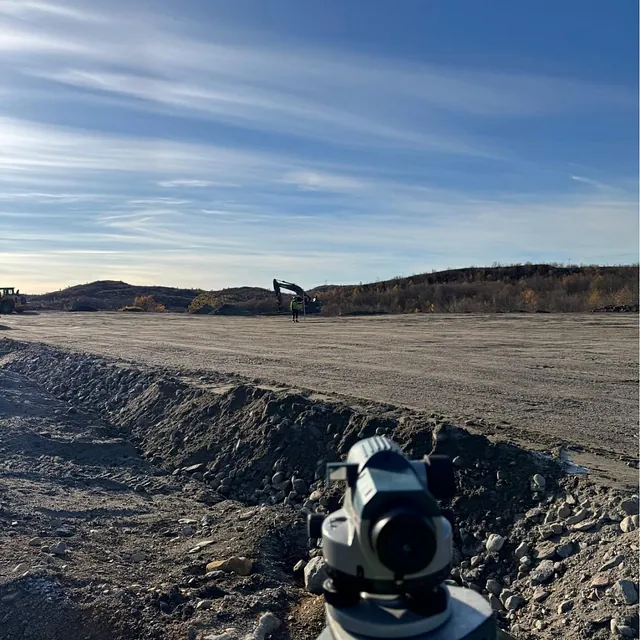 Måleinstrument i forgrunnen med anleggsarbeid i horisonten på stort flatt område.